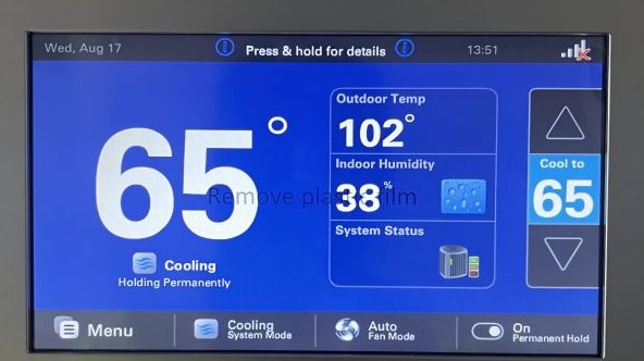 Trane thermostat showing 65°F indoor with 102°F outdoor — the money shot